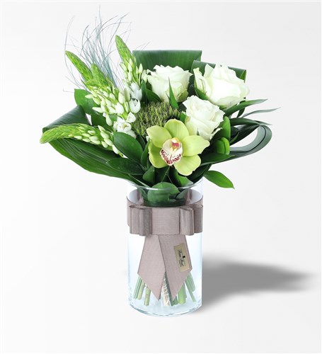 Flower arrangement of white roses and orchids in a cylindrical glass vase.