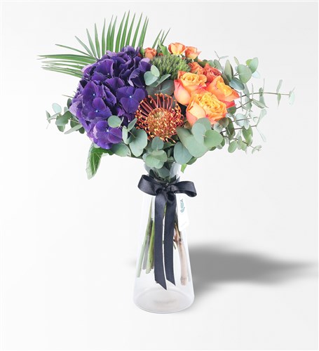 Arrangement of purple hydrangeas and orange roses in a black glass vase.