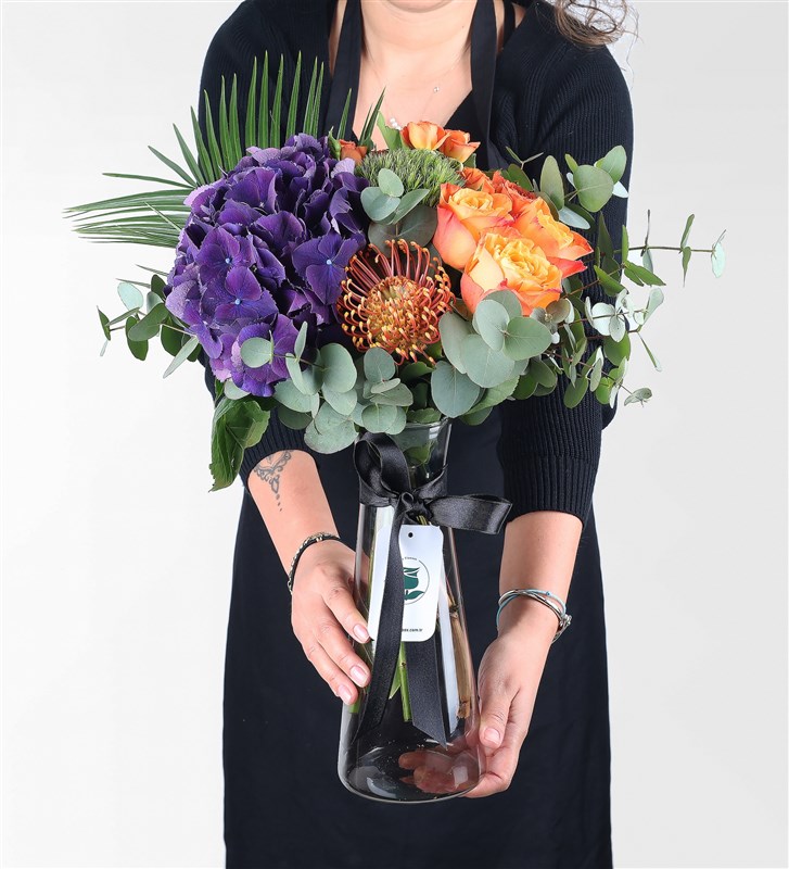 Arrangement of purple hydrangeas and orange roses in a black glass vase.
