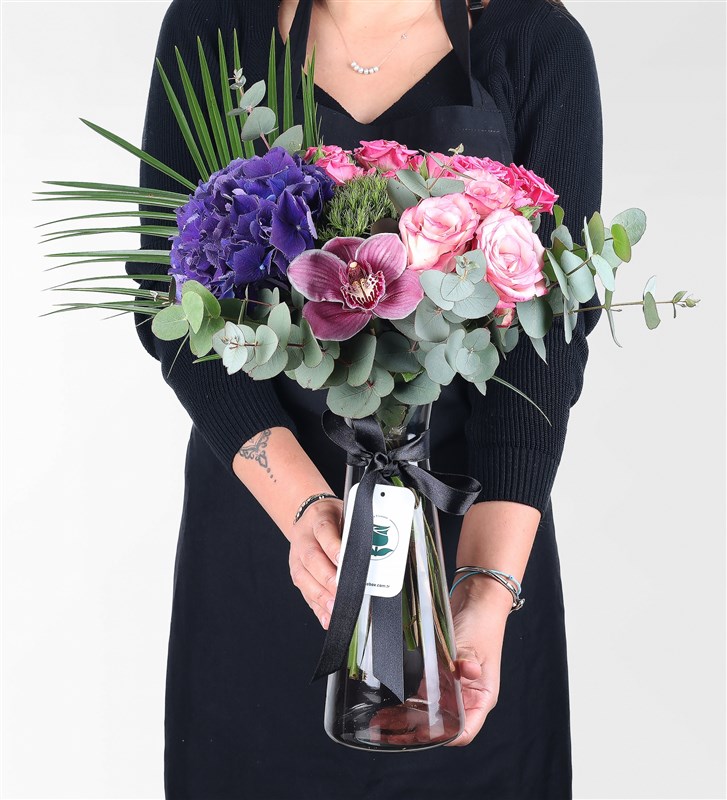 Arrangement of purple hydrangeas, roses, and orchids in a black glass vase.