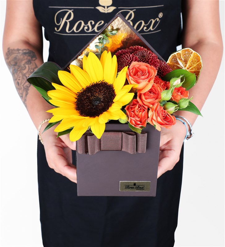 Sunflower arrangement in a brown box with orange rose bushes.