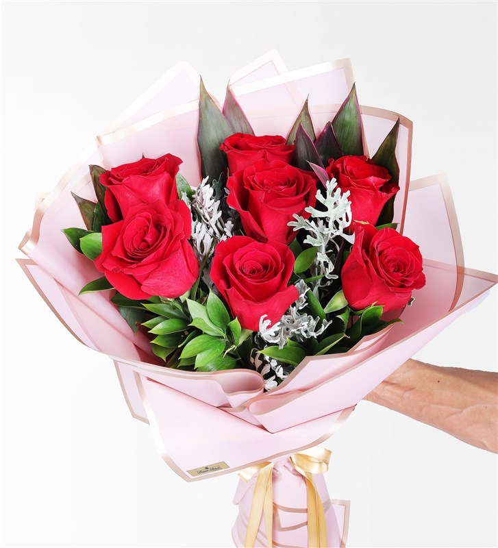 A bouquet of 7 red roses, cordyline, and wormwood in a pink-trimmed package.